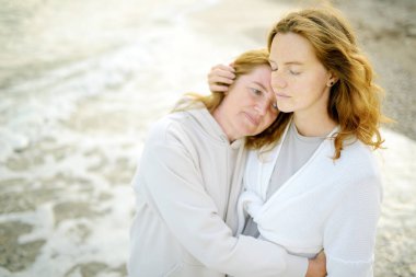 Kızıl saçlı kıdemli anne ve güzel yetişkin kızı birlikte yürüyorlar ve kucaklaşıyorlar. Bir anne ve yetişkin çocuğunun mutlu bir buluşması. Yetişkin çocuklar ve yaşlı ebeveynler arasındaki aile ilişkileri