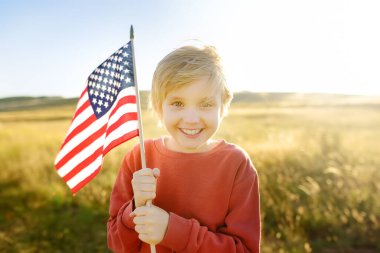 Cute little boy celebrating of July, 4 Independence Day of USA at sunny summer sunset. Child running with american flag of United States on wheat field. Proud little american boy holding country flag