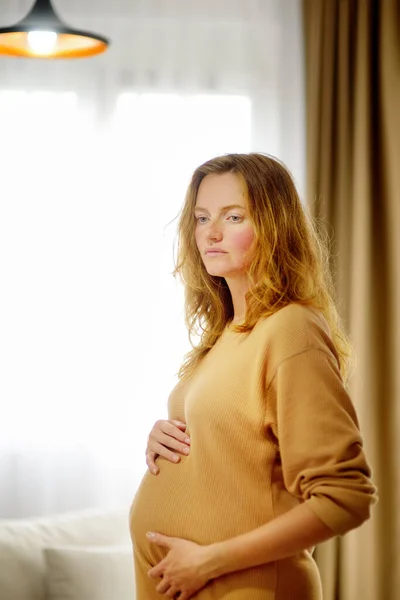 怀孕的高加索女人在家里放松 年轻的孕妇抚摸着怀孕的肚子 想着分娩的事 母亲和怀孕的概念 — 图库照片