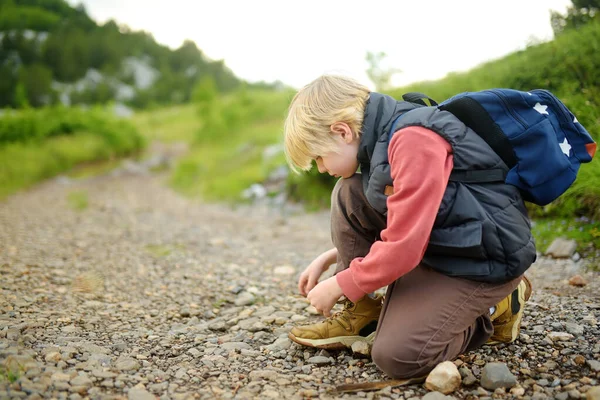 在山区山谷的路上追踪时 一个未成年男孩正在系鞋带 和孩子一起远足的家庭积极的生活方式 随遇而安 — 图库照片