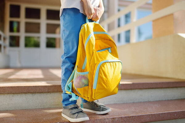 Little student with a backpack on the steps of the stairs of school building. Close-up of child legs, hands and schoolbag of boy standing on staircase of schoolhouse. Kids back to school concept.