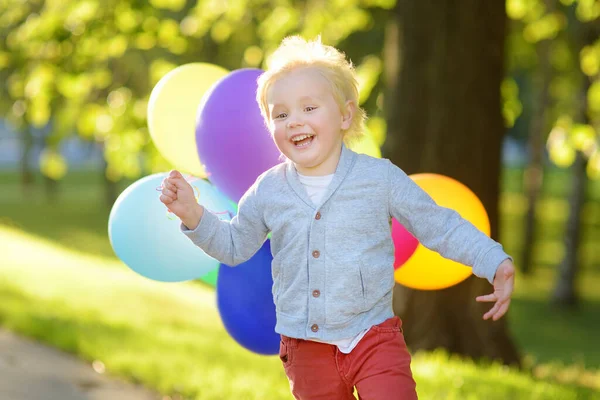 誕生日パーティーを楽しむ男の子 明るい多色の風船の束を持つ幸せな子供 日当たりの良い公園で幼児や幼児の誕生日パーティー 子供のための夏の屋外フェスティバル — ストック写真
