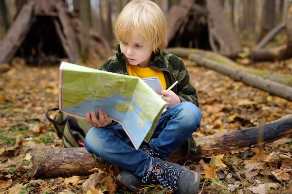 小男孩侦察兵正在森林里探路 孩子们正坐在倒下的树上 从地图上俯瞰着茅屋的背景 儿童探险 探险及远足旅游的概念 — 图库照片