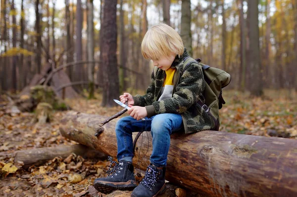 小男孩的侦察员正在森林里用小刀削尖一根棍子 儿童探险 探险及远足旅游的概念 — 图库照片