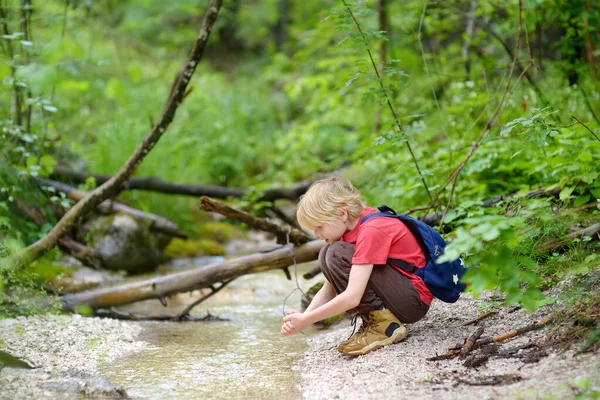 赤いシャツの前の少年は 山の谷のハイキング中に小川の水で自然を探索し 遊んでいます 精力的な子供のためのアクティブなレジャー 子供のためのサマーキャンプ屋外レクリエーション — ストック写真