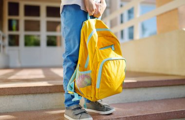 Little student with a backpack on the steps of the stairs of school building. Close-up of child legs, hands and schoolbag of boy standing on staircase of schoolhouse. Kids back to school concept.