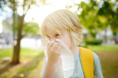Çocuk hapşırıyor ve yaz parkında yürürken burnunu peçeteyle siliyor. Alerjik çocuk. Hasta çocuklar. Grip mevsimi ve soğuk algınlığı tedavileri