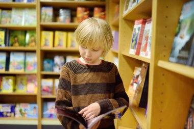 Okul kütüphanesinde ya da kitapçıda kitap raflarında dikilirken kitap sayfalarını karıştıran bir çocuk. Akıllı çocuk çizgi roman ya da macera kitabı okuyor.