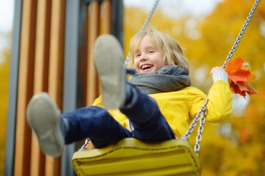 Küçük çocuk sonbahar günü halk parkında salıncakta sallanırken eğleniyor. Mutlu çocuk sallanmaktan zevk alır. Şehirde çocuk için aktif açık hava eğlencesi