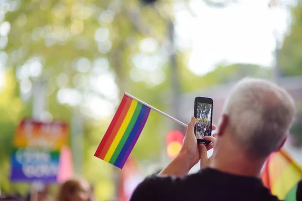 Man activist with rainbow flag taking a picture using smartphone of march during the Pride Parade. Fight for equal rights. Rainbow flag is symbol of Lgbt