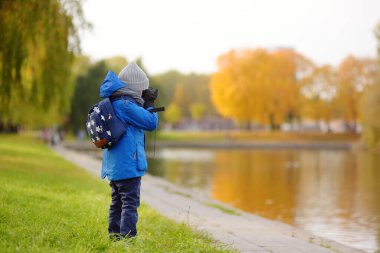 Küçük çocuk güneşli sonbahar gününde şehir parkında gezinirken eğleniyor. Çocuk dürbünle doğayı keşfediyor. Çocuklarla dışarıda ailece vakit geçirmek. Güzel modern şehir parkı.