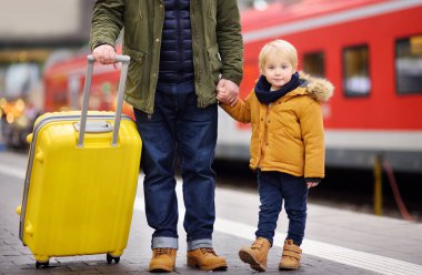 Küçük boy gülümseyerek ve babası tren istasyonu platformu üzerinde hızlı tren bekliyor. Seyahat, turizm, kış tatili ve aile kavramı. Adam ve oğlu birlikte.