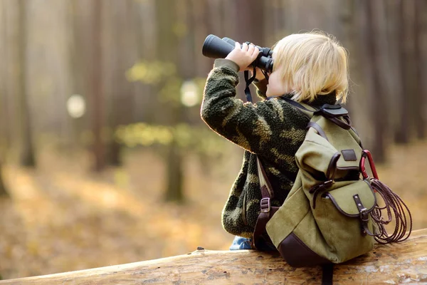 秋の森の中でハイキング中に双眼鏡を持つ小さな男の子のスカウト 子供たちは大きな倒木の上に座って双眼鏡を見ています 子供のための冒険 スカウティング ハイキング観光の概念 — ストック写真