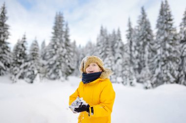 Çocuk Avrupa Alpleri 'nde tatil sırasında taze karla oynarken eğleniyor. Sıcak kıyafetler, şapka, eldiven ve eşarp giymiş bir çocuk. Tatil zamanı çocuklar için açık havada aktif bir kış tatili