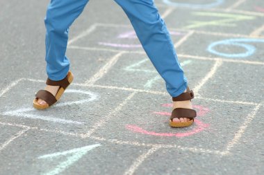 Küçük çocuğun bacakları ve asfalta çizilmiş seksek viskisi. Çocuk bahar günü oyun bahçesinde seksek oynuyor. Çocuklar için açık hava aktiviteleri.