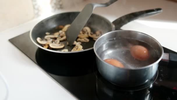 中年男人做早餐的特写视频 在小锅里煮熟的鸡蛋和油炸蘑菇作为健康的一餐 — 图库视频影像