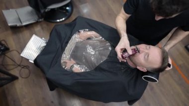 Berber ustası, kuaförde sakallı yakışıklı bir adamı tıraş ediyor. Berber dükkanında sakal ve bıyık modelliği yapan bir kuaför. Profesyonel stilistin hizmetleri. Erkekler için moda saç bakımı