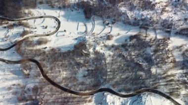 Kışın manzaralı dağlar arasındaki yolda insansız hava aracından inanılmaz bir manzara. Uzağa doğru uzanan resimsel bir dağ yılanının yukarıdan görünüşü. Arabalar dolambaçlı bir yol boyunca gider.
