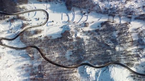 冬の風光明媚な山間の道路上の無人機からの素晴らしい空中視界 遠くに伸びる美しい山の蛇のトップダウンビュー 風向きのハイウェイを走行する車両 — ストック動画