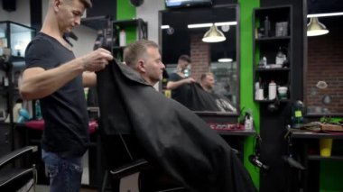 Berber ustası, yakışıklı, olgun, sakallı bir müşteriyi kuaförde saç tıraşına başlaması için hazırlıyor. Berber dükkanında sakal ve bıyık modelliği yapan bir kuaför. Profesyonel stilin hizmetleri