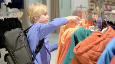Ergenlik çağındaki güzel bir çocuk mağazada kendine mevsimlik sıcak kıyafetler seçer. Çocuklu aile alışverişi. Bağımsız bir çocuk alışveriş merkezinde annesine yardım eder.