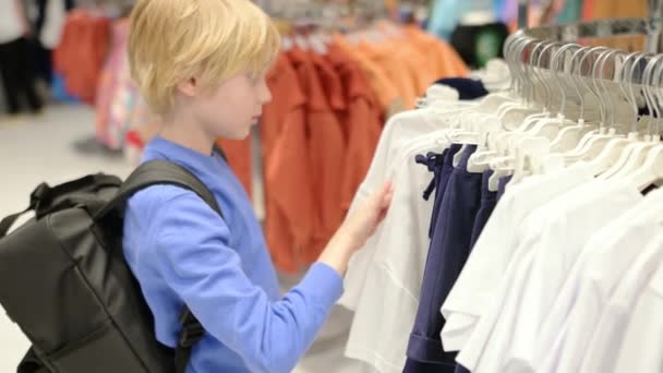 かわいい年齢の男の子は 店で自分自身のためにファッション服を選択します 子供と家族のためのショッピング 独立した子供がショッピングモールで母親を助ける — ストック動画