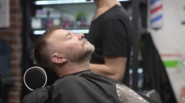 Berber ustası, kuaförde sakallı yakışıklı bir adamı tıraş ediyor. Saç sanatçısı berber dükkanında sakal modelliği yapıyor. Profesyonel stilistin hizmetleri. Erkekler için moda saç bakımı