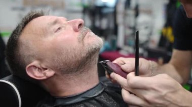 Berber ustası, kuaförde sakallı yakışıklı bir adamı tıraş ediyor. Saç sanatçısı berber dükkanında sakal modelliği yapıyor. Profesyonel stilistin hizmetleri. Erkekler için moda saç bakımı