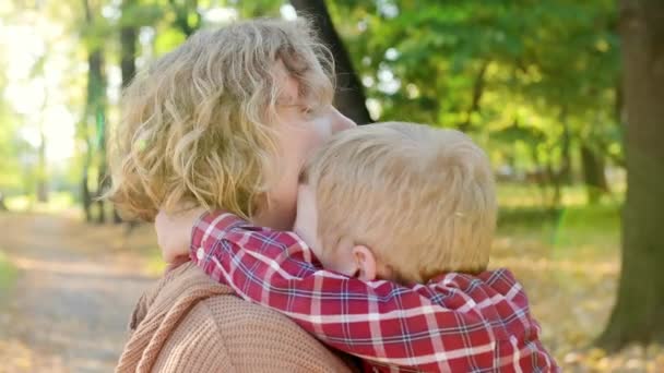 在秋天公园散步时 一对母子的特写视频 女人把她那蹒跚学步的儿子抱在怀里 温柔地拥抱他 一个小男孩和他的妈妈玩得很开心 — 图库视频影像