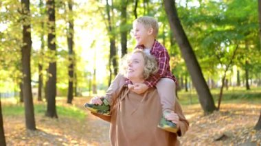 Anne ve oğlu sonbahar parkında birlikte eğleniyorlar. Güzel bir kadın küçük çocuğunu omuzlarında taşır. Çocuklu aileler için geleneksel mevsimsel etkinlik