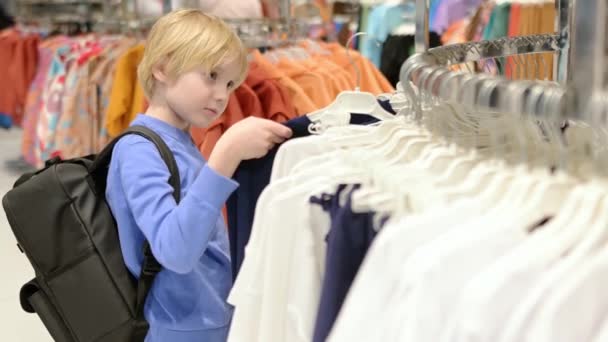 一个漂亮的十几岁的男孩在商店里为自己选择服装 为有孩子的家庭购物 一个独立的孩子在购物中心帮助他的母亲 — 图库视频影像