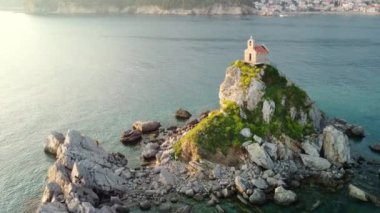 Karadağ 'ın Petrovac kenti yakınlarındaki Sveta Nedjelja Adası' nın insansız hava aracından inanılmaz bir gün batımı görüntüsü. Resimli taş ada ve Adriyatik deniz dalgalarıyla çevrili bir uçurumda küçük bir kilise.