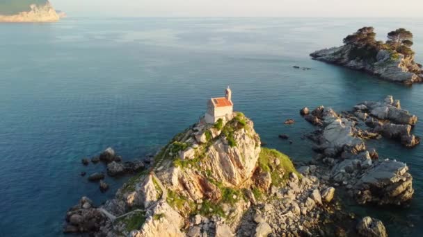 モンテネグロのペトログラフ近くの小さな教会ネドルジャ島の無人機からの驚くべき日没の空中眺め 美しい石の島とアドリア海の波に囲まれた崖の上の小さな教会 — ストック動画