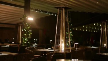 Kışın gaz sobası olan samimi bir açık hava restoranı. Gece vakti yanan ateş olan bir kafe avlusunun dışında. Sıcak Noel arifesi sahnesi.