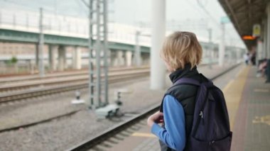 Sevimli bir genç çocuk tren istasyonunda ya da metro istasyonunda tren bekliyor. Metropolis ulaşım sistemi. Büyük bir şehirde toplu taşıma