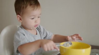 Sabahleyin mutfakta sağlıklı bir kahvaltılık gevrek yiyen tatlı bir çocuk. Bir bebek kaşıkla yemek yemeyi öğreniyor. Tamamlayıcı beslenme, çocuğun beslenmesinde yeni bir aşamadır..