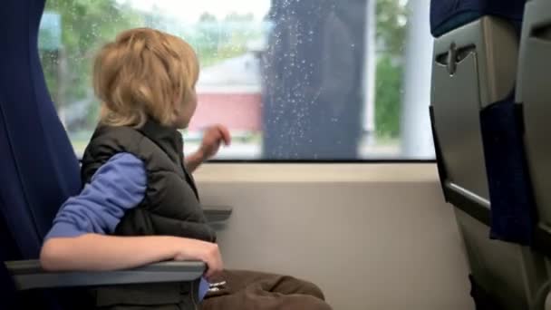 可爱的未成年男孩在外面下雨的时候乘坐当地的火车或铁路旅行 儿童乘客的肖像 — 图库视频影像