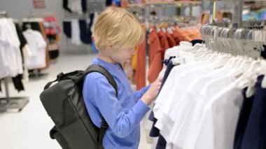 Ergenlik çağındaki güzel bir çocuk mağazada kendisi için moda kıyafetleri seçer. Çocuklu aile alışverişi. Bağımsız bir çocuk alışveriş merkezinde annesine yardım eder.