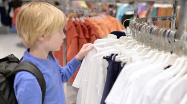 Ergenlik çağındaki güzel bir çocuk mağazada kendisi için moda kıyafetleri seçer. Çocuklu aile alışverişi. Bağımsız bir çocuk alışveriş merkezinde annesine yardım eder.