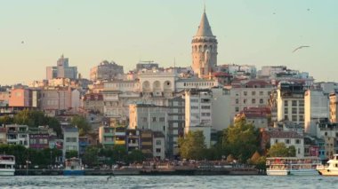 İstanbul, Türkiye - 6 Ağustos 2023: Günbatımında köprüye yakın Golden Horn sahil şeridinin manzarası. Çok uzakta ünlü Galata Kulesi var. İstanbul 'un güzel, yoğun şehir manzarası. Önünde martılar var.