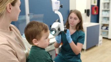 Annesiyle birlikte tatlı bir çocuk anaokuluna hazırlanmak için pediatrik bir KBB ile randevuda. Doktor otolaringolog ENT mikroskobu altında küçük bir hastanın kulağını inceliyor.