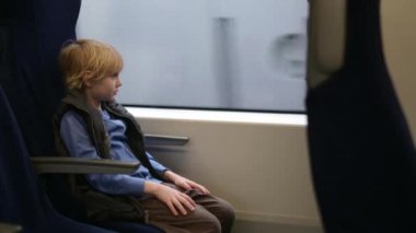 Tatlı çocuk dışarıda yağmur yağarken yerel bir tren vagonunda ya da demiryolunda seyahat ediyor. Çocuk yolcu portresi.