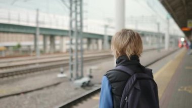 Sevimli bir genç çocuk tren istasyonunda ya da metro istasyonunda tren bekliyor. Metropolis ulaşım sistemi. Büyük bir şehirde toplu taşıma