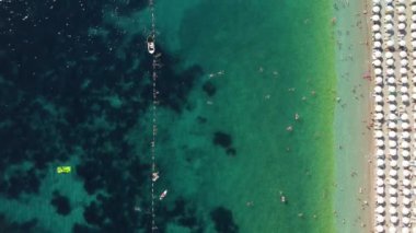 Sıcak bir yaz gününde insanlarla dolu bir plajın insansız hava görüntüsü. Tatil sezonu. Mükemmel kumlu bir sahilde beyaz güneş şemsiyeleri üst üste. En saf şeffaf Adriyatik Denizi