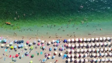 Sıcak bir yaz gününde insanlarla dolu bir plajın insansız hava görüntüsü. Tatil sezonu. Mükemmel kumlu bir sahilde beyaz güneş şemsiyeleri üst üste. En saf şeffaf Adriyatik Denizi