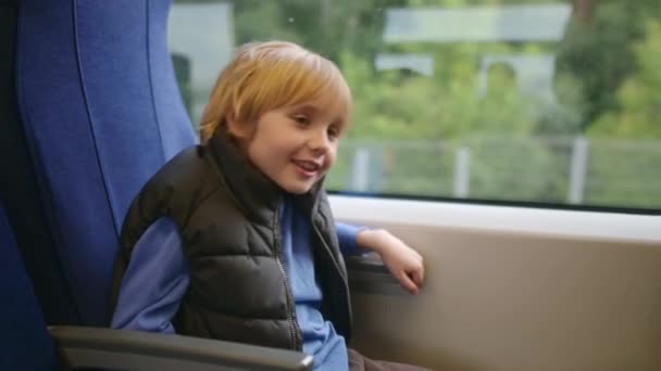 可爱的未成年男孩在外面下雨的时候乘坐当地的火车或铁路旅行 儿童乘客的肖像 — 图库视频影像