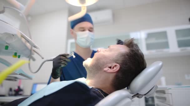 医療センターでの歯医者と患者 医者は歯科ツールを使用して成熟した男の歯のための専門的な口腔衛生を行います 歯科衛生士による深い歯の洗浄手順 — ストック動画