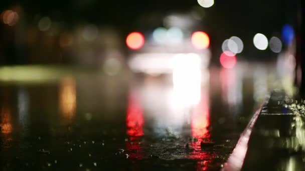 夜市での暴風雨の大気ビデオ 低点から撮影された水たまりを通過する車からの大雨とスプラッシュ 街灯の光の中で舗装上の大きな滴が壊れます スローモーション ストック動画