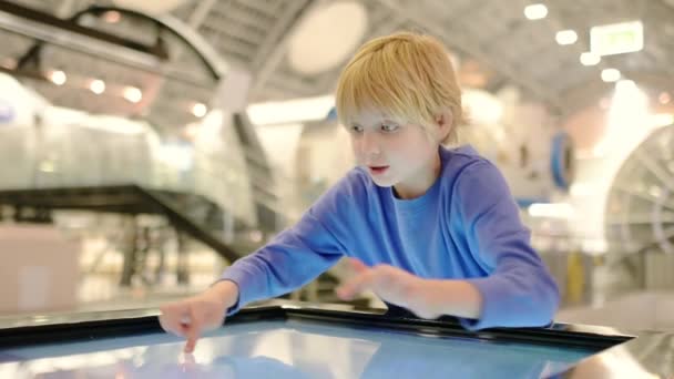 サイエンスミュージアムを訪れる小学生の子供 少年はインタラクティブなタッチスクリーンディスプレイでの展示に関する情報を探しています ストック動画