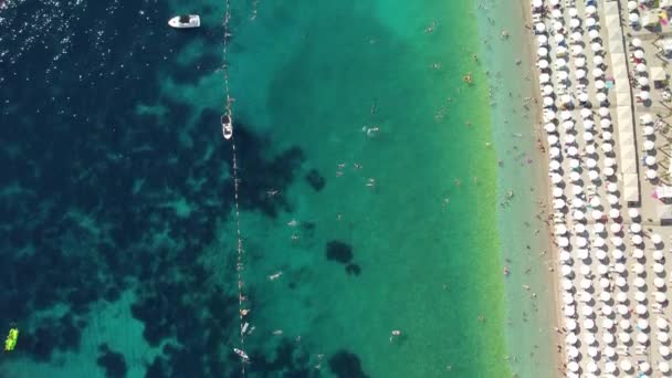 炎热的夏天 俯瞰着一个挤满了人的海滩 假日旺季 在一个完美的沙滩上 一排排白色的遮阳伞 最纯净透明的亚得里亚海 免版税图库视频